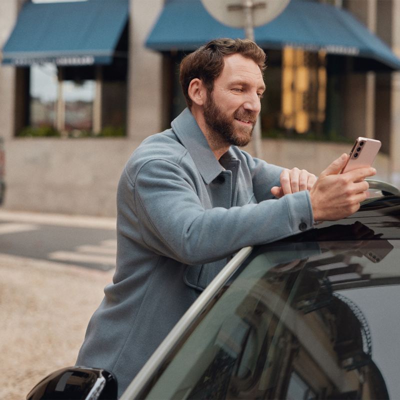 a man on his mobile phone in public leaning against a Volkswagen