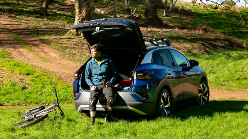 a man leaning against the open boot of a dark blue ID.4 in the countryside