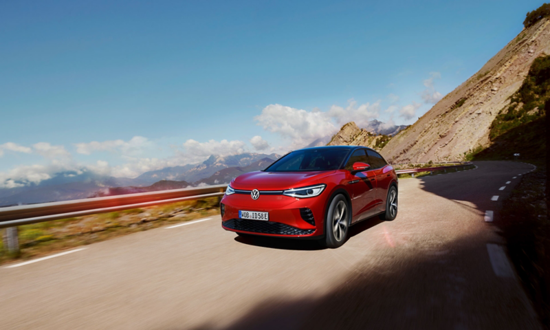 Red VW ID.5 GTX drives dynamically on a mountain road. View of front, wheels and side.