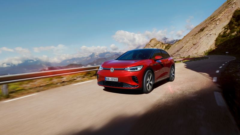 Red VW ID.5 GTX drives dynamically on a mountain road. View of front, wheels and side..