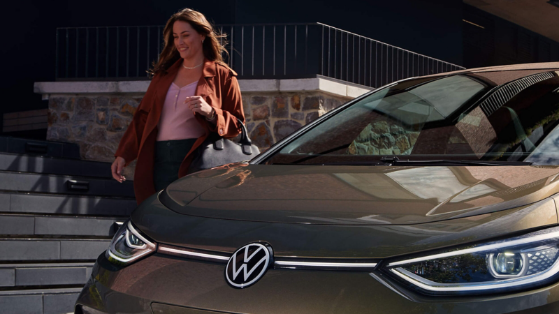 A woman walking beside a parked VW car