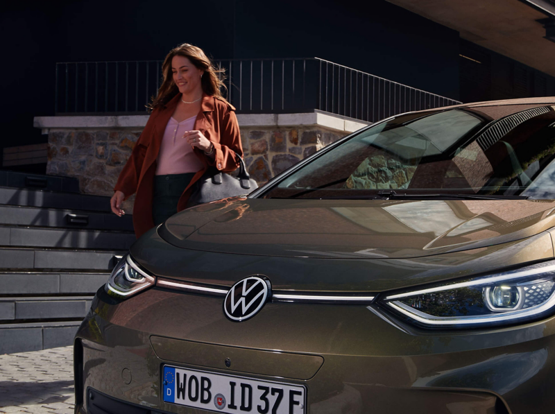 A woman walking beside a parked VW car