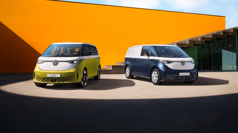 Two VW ID. Buzz vans parked next to each other in front of an orange building. 