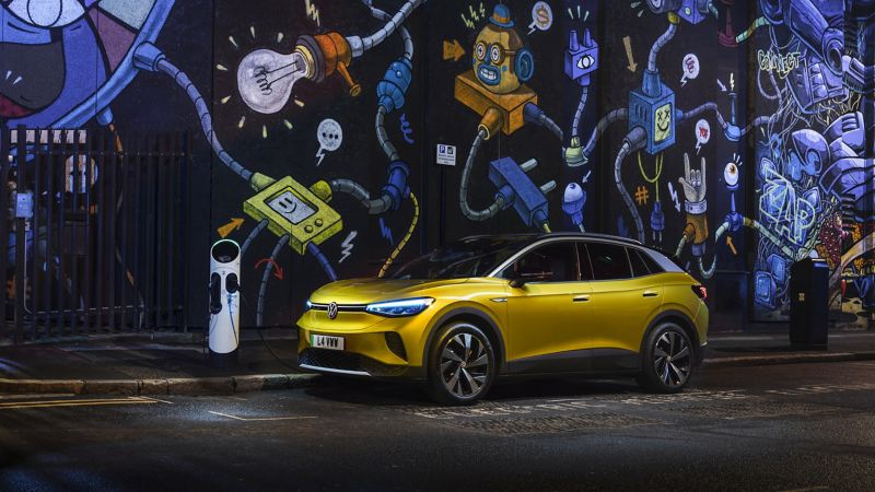 An ID.4 parked in front of a graffitied wall at a charging station