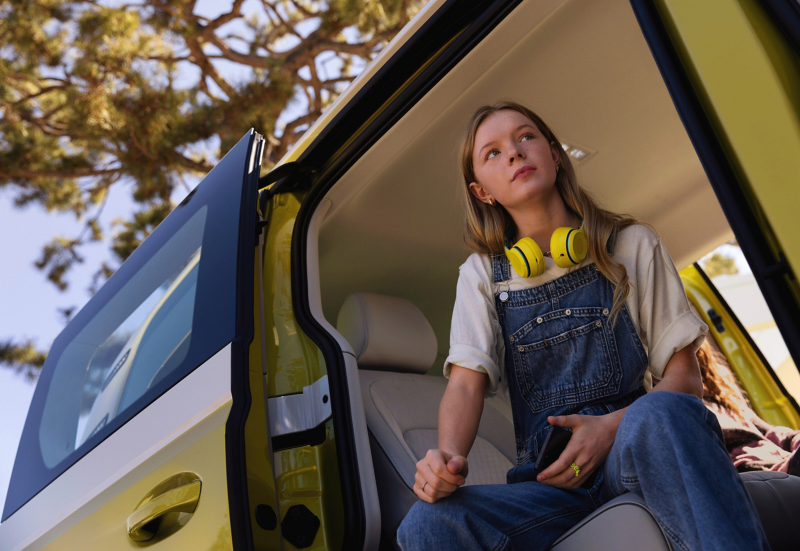 A girl with yellow headphones sits in the side door of the VW ID. Buzz.