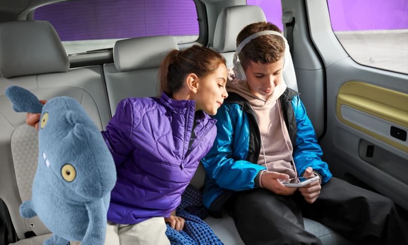 A brother and sister sat on the back seat of an ID.Buzz playing on an electronic device