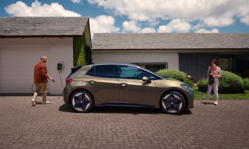 A view of a VW ID.3 in “Dark Olivine Green Metallic” parked on a driveway with a man plugging in the charger