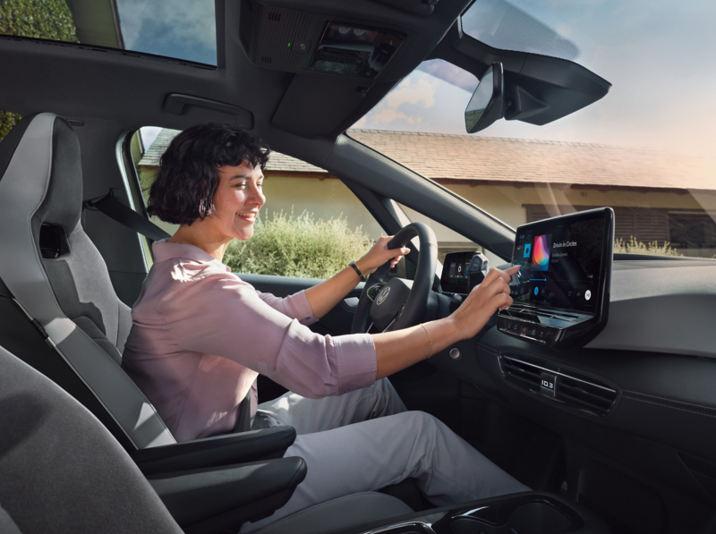 A woman sitting inside a VW  ID. car and operating the touchscreen