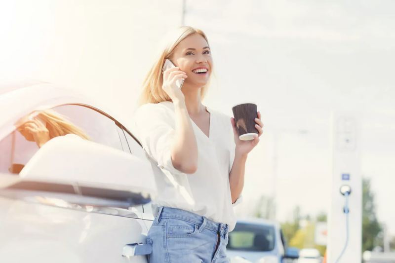 Woman standing beside a car on the phone drinking coffee