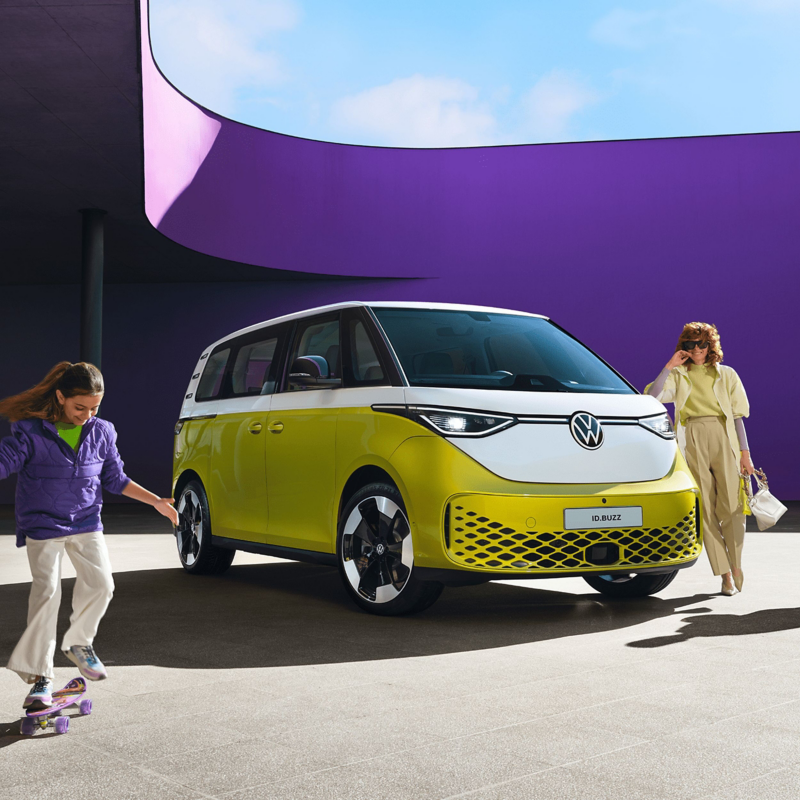 A woman standing and a young girl on a skateboard next to a yellow ID. Buzz. 