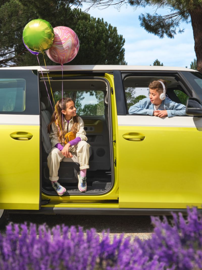 ID. Buzz parked at a house with children holding baloons sitting inside it. 