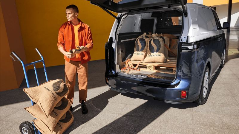 Person loading VW ID. Buzz cargo with large coffee sacks