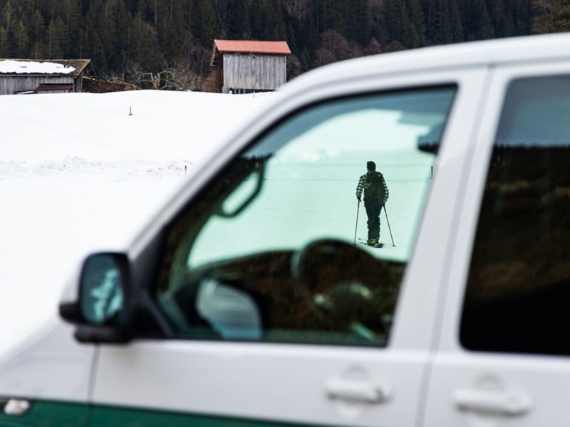 Vit och grön VW Transporter. Genom rutan syns en man som åker skidor.