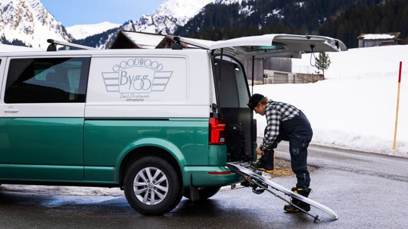 Man står bakom en VW Transporter och snörar på sig snowboardkängor
