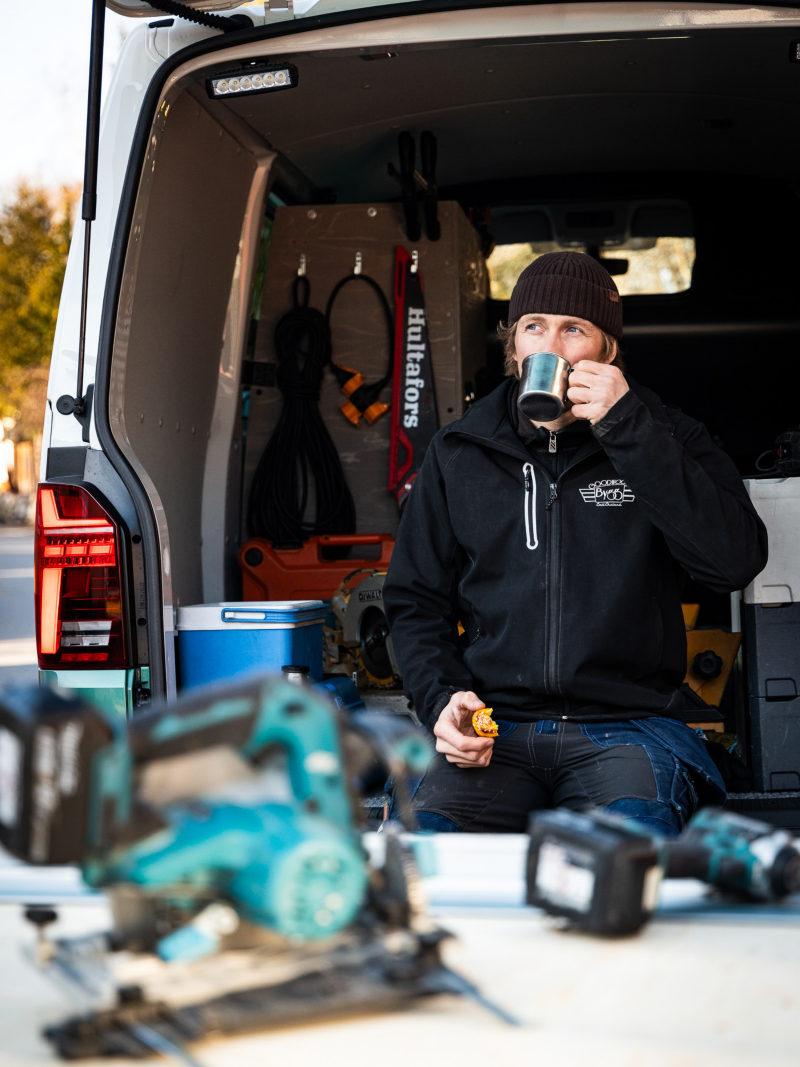Man sitter i lastutrymmet på en VW Transporter och fikar