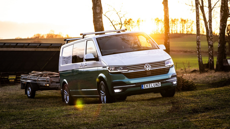 Vit och grön VW Transporter kör i solnedgången med ett släp bakom sig
