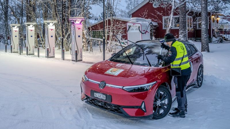 Ein ID.7 GTX Tourer steht im Schnee neben einer Ladesäule