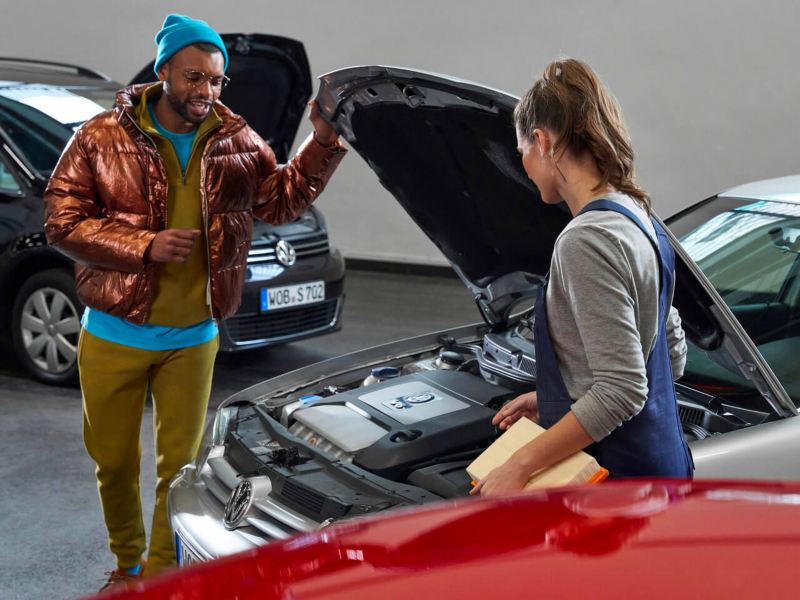 Une technicienne Volkswagen et un client discutent dans un atelier, entourés de véhicules Volkswagen.