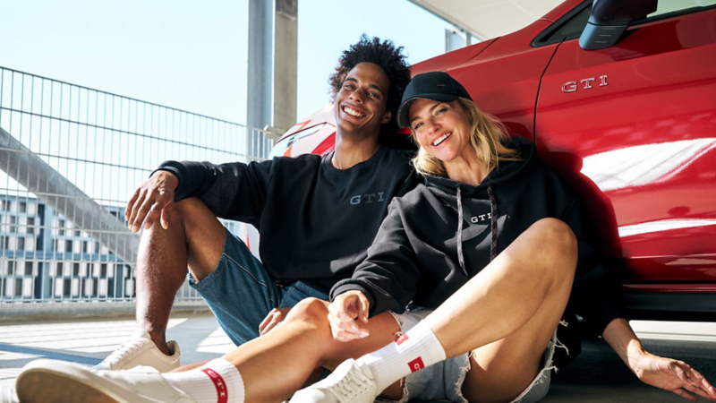 Un apareja con sudaderas GTI sentada junto a un Volkswagen rojo
