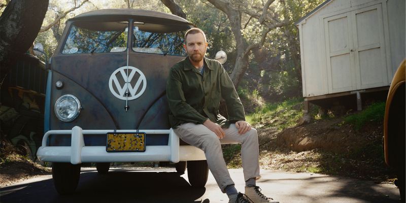 Volkswagen Markenbotschafter Ewan McGregor sitzt auf der Stoßstange seines VW Bulli. 