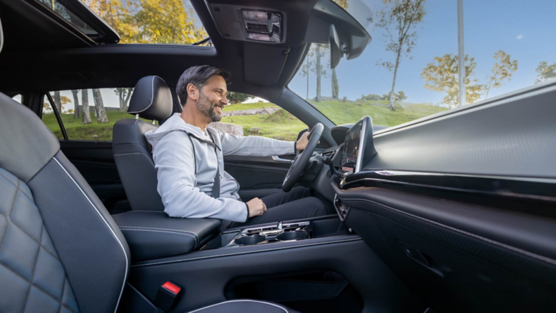 Conductor sonríe al manejar una camioneta de Volkswagen con techo panorámico abierto.