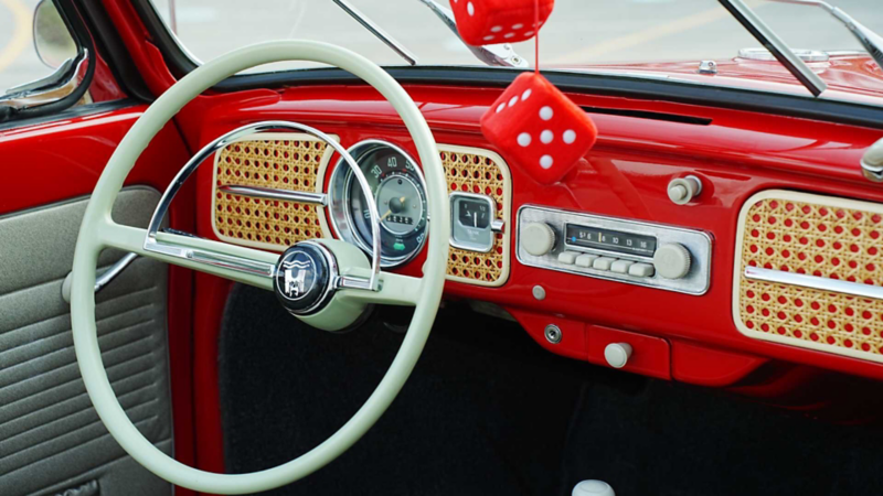 Interior de Volkswagen sedan clásico rojo muestra volante y tablero con dados.