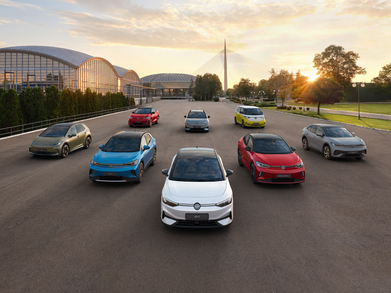 Wide shot of multiple colorful Volkswagen electric vehicles parked in a V-formation outdoors at sunset.