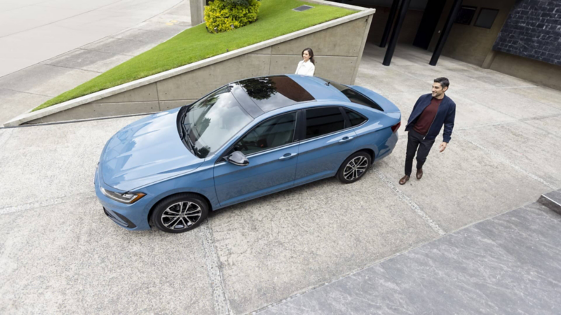 Pareja camina hacia puertas de Jetta 2025, edición Sportline en color azul.