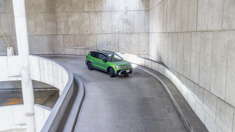 Taos VW verde en una rampa curva de concreto con barreras blancas, visto desde arriba.