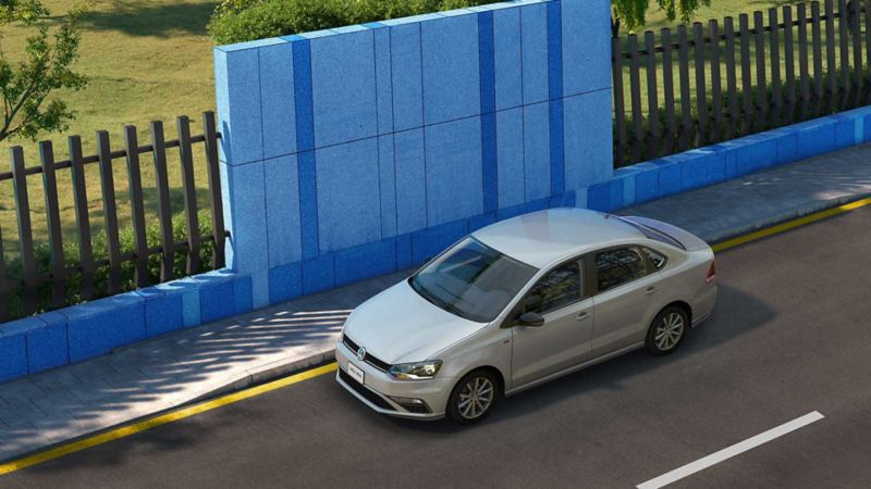 Vento Join de Volkswagen. Auto sedán gris estacionado en la calle, cerca de muro azul.