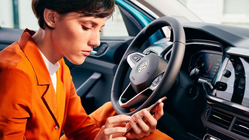 Une femme consulte son smartphone, assise dans sa voiture Volkswagen.