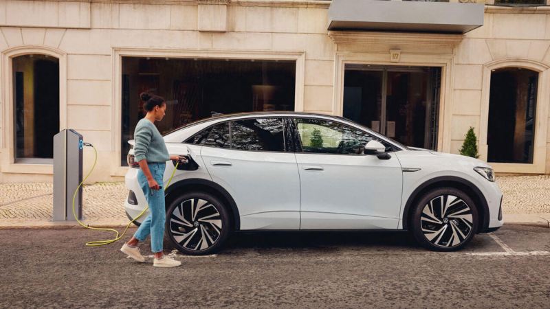 Une femme recharge son Volkswagen ID.5 blanc sur une borne dans la rue.