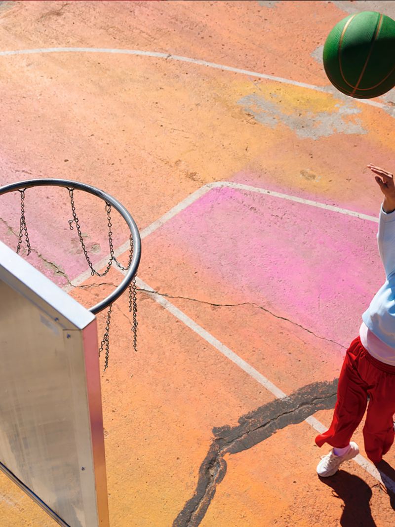 A woman in an urban setting throws a basketball towards a basket. Lifestyle.