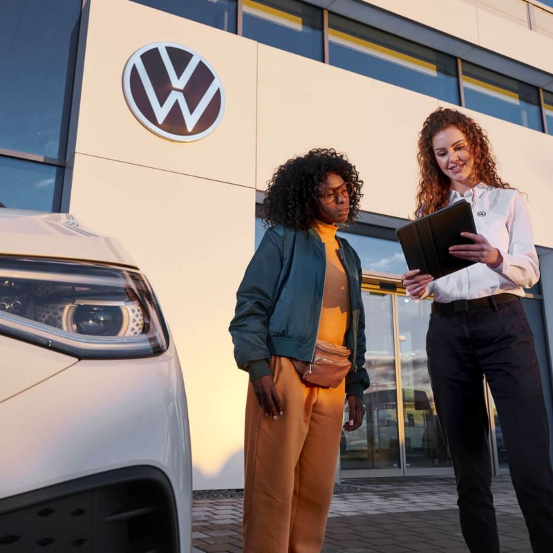 Une femme et une conseillère Volkswagen discutent devant une concession.