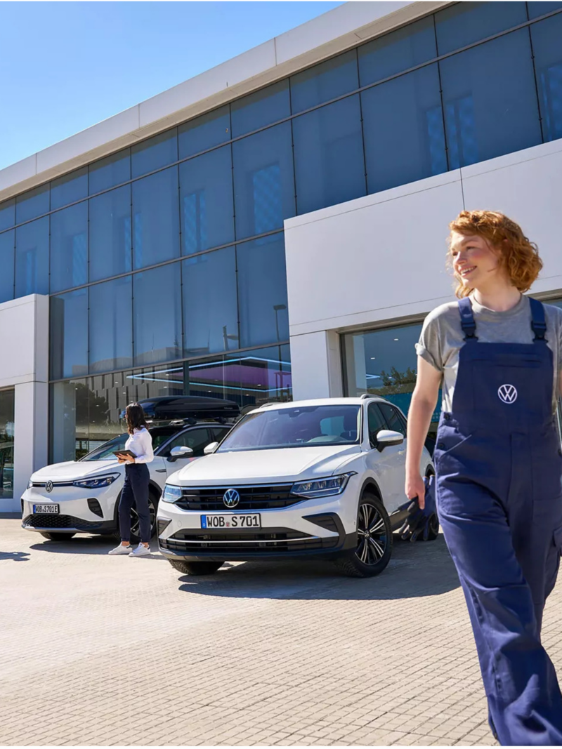 A Volkswagen retailer building with a service employee and white VW SUVs parked outside.