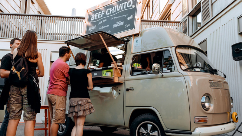 Gäste bestellen Speisen an einem Foodtruck mit Volkswagen Oldtimer.