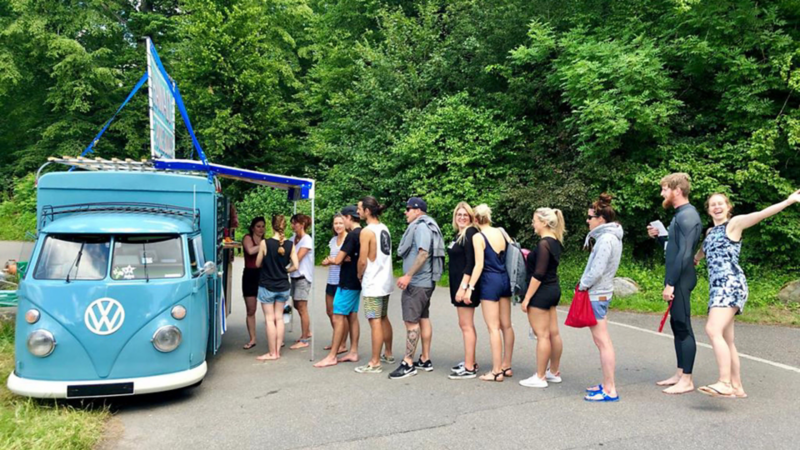 Besucherinnen und Besucher vor einem Foodtruck mit Volkswagen Oldtimer.