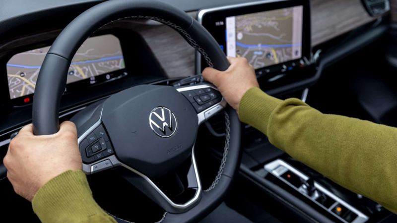 Conductor toma el volante de un auto volkswagen con pantallas digitales.