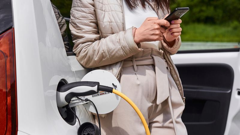 Eine Frau steckt einen Ladestecker mit gelbem Kabel in ein weißes Elektroauto.