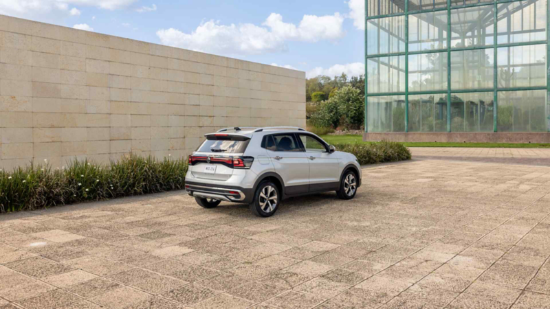 Volkswagen Taigun. SUV color plata estacionado frente a edificio moderno con paredes de cristal y muro de cantera.