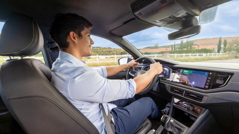 Conductor toma el volante de un auto Volkswagen mientras conduce por un potrero. 