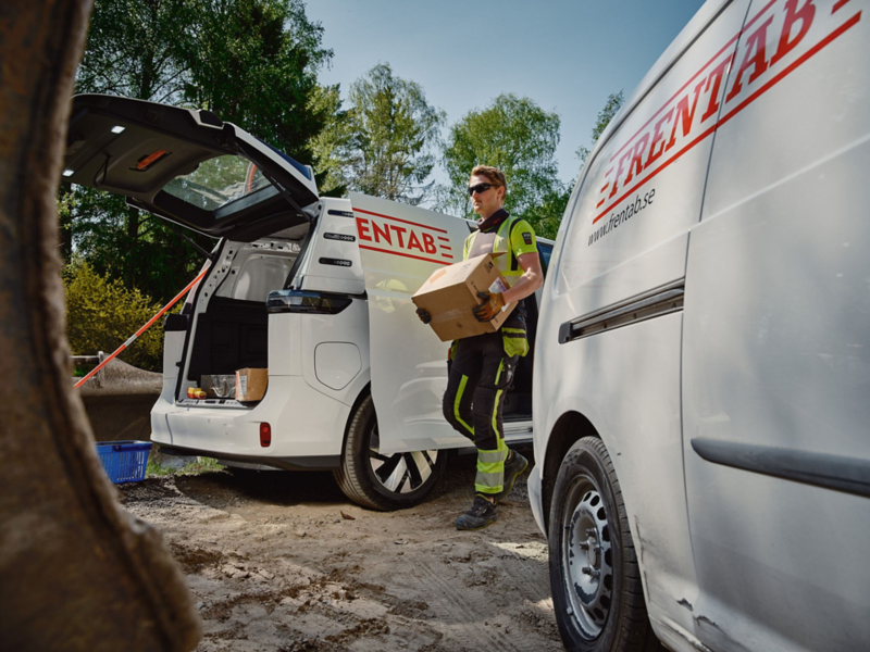 Man går med låda mellan två modeller från VW transportbilar