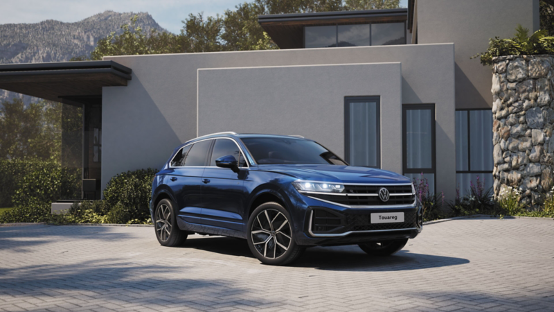 A VW Touareg R-Line parked at the roadside, diagonal view from above of the rear and panoramic sunroof.