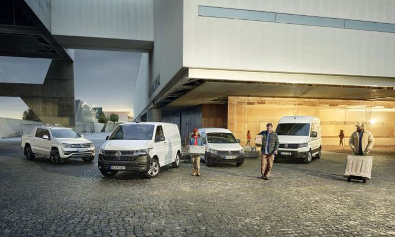 Tre lavoratori si allontanano con alcuni pacchi da quattro veicoli commerciali Volkswagen: Amarok, Transporter Furgone, Nuovo Caddy Cargo e Crafter Furgone.