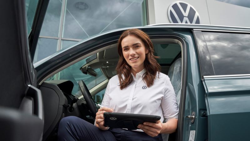 Una agente de servicio sonriendo apoyada en la silla del piloto en un Volkswagen