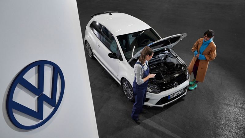Agente de servicio y una cliente junto a un Volkswagen con el capó abierto
