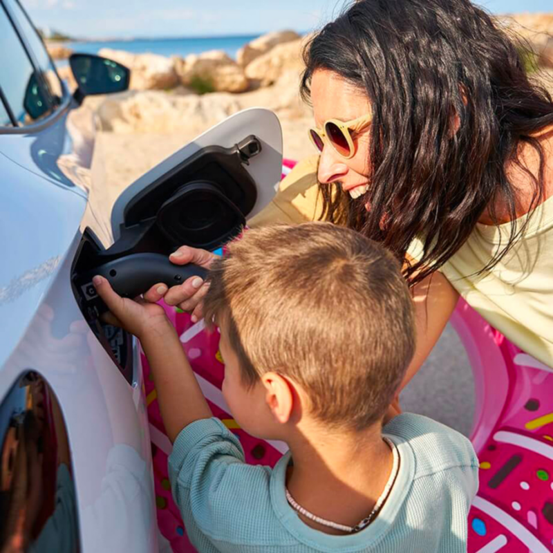 Inquadratura di una madre mentre mostra al figlio come inserire nell'auto la pompa di benzina.