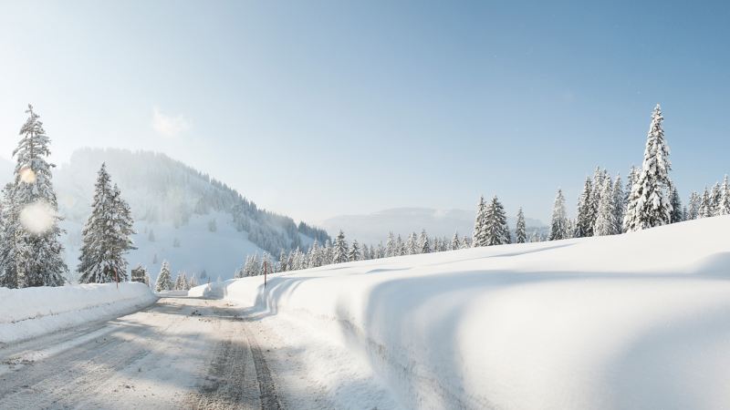 Eine geräumte Straße führt durch eine verschneite Winterlandschaft.