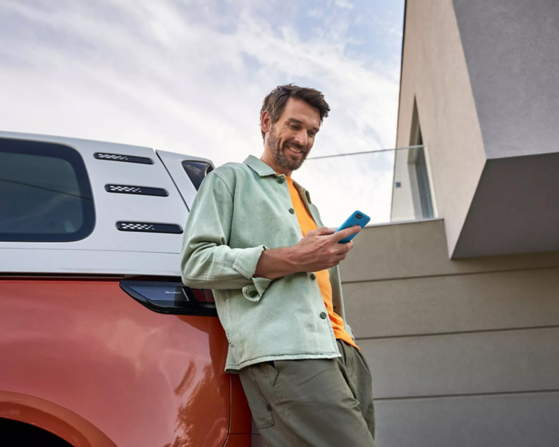 Man leaning against electric vehicle with mobile phone.