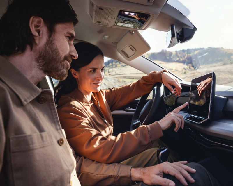 A man and woman inside a VW car view a navigation screen amid mountains.